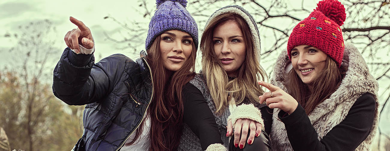 Happy tree girls wearing a woolly hats and showing something